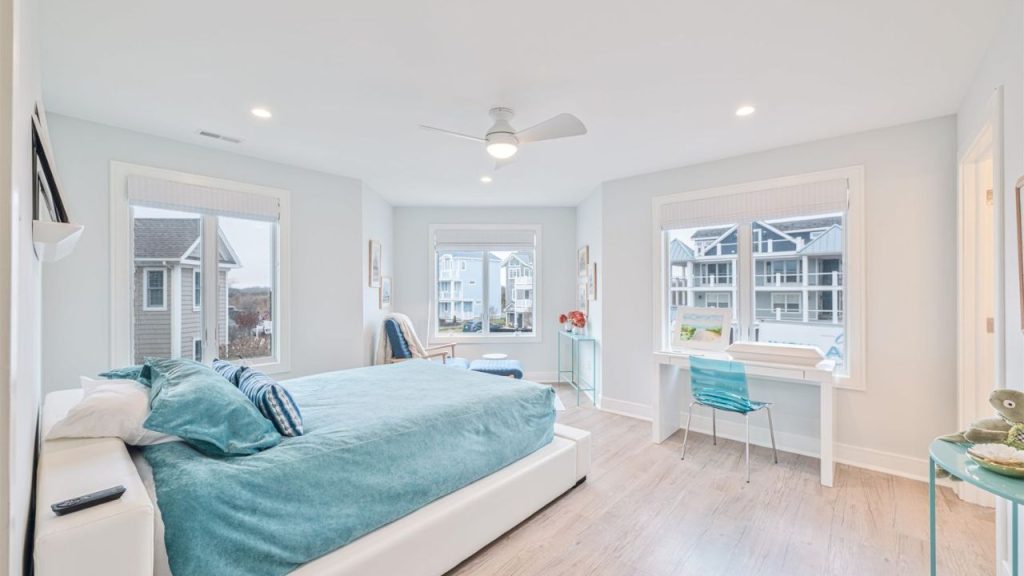 A bright coastal bedroom with blue decor, large windows, and a reading nook.