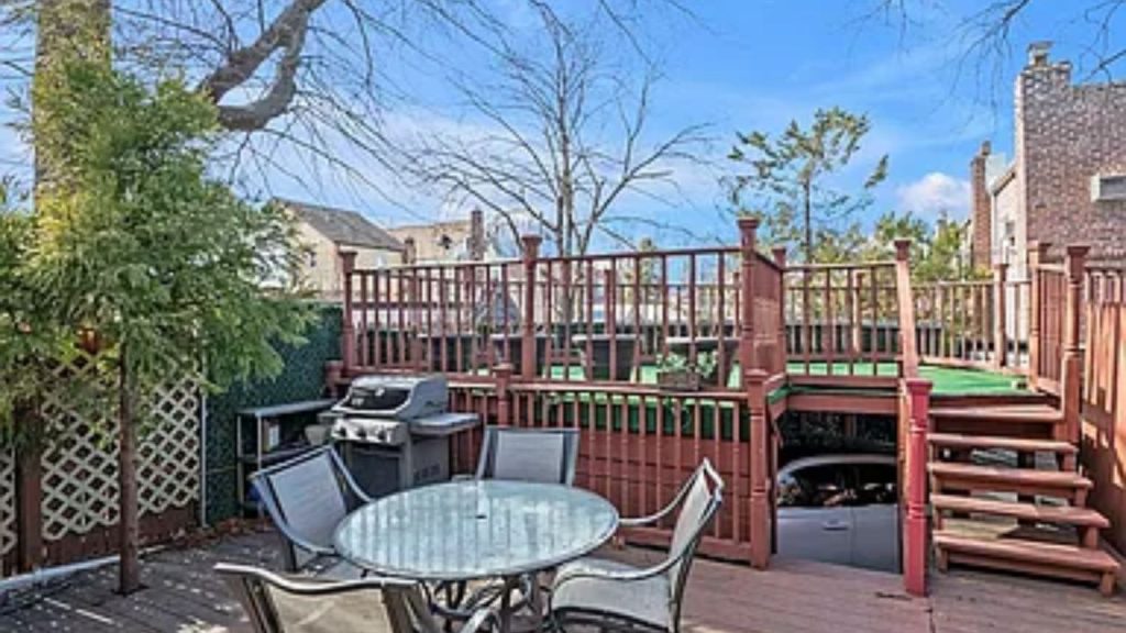 A multi-level backyard deck with a grill, dining set, and covered parking.