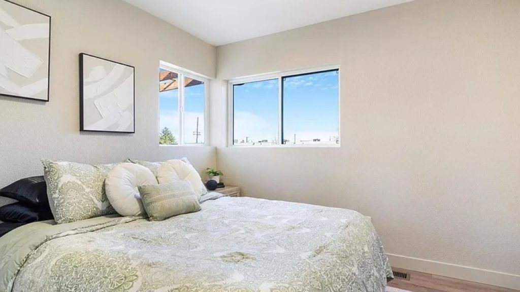 Bright bedroom with large windows, soft green bedding, and modern decor.