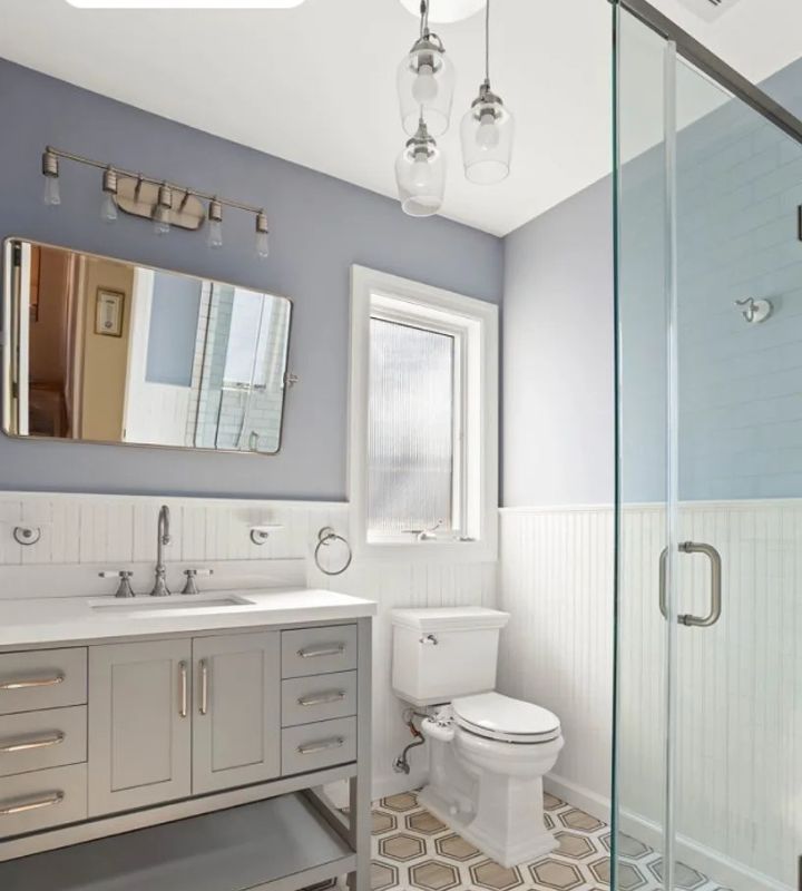A bright and airy bathroom with soft lavender walls, a sleek vanity, and a glass-enclosed shower.