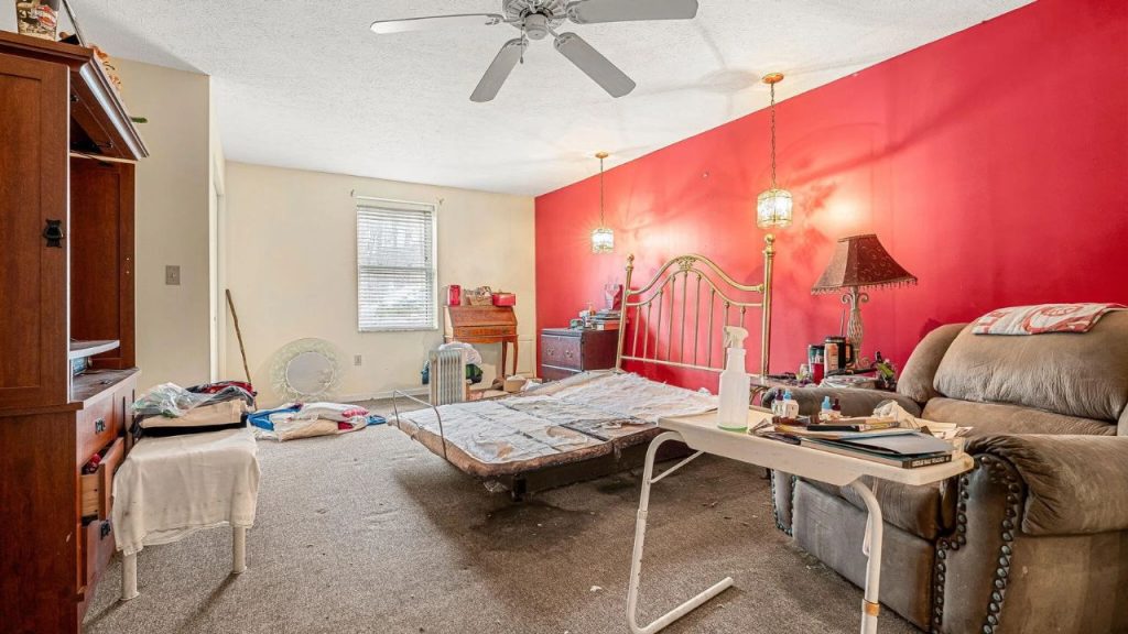 Large bedroom with a red accent wall, brass bed frame, and recliner chair.