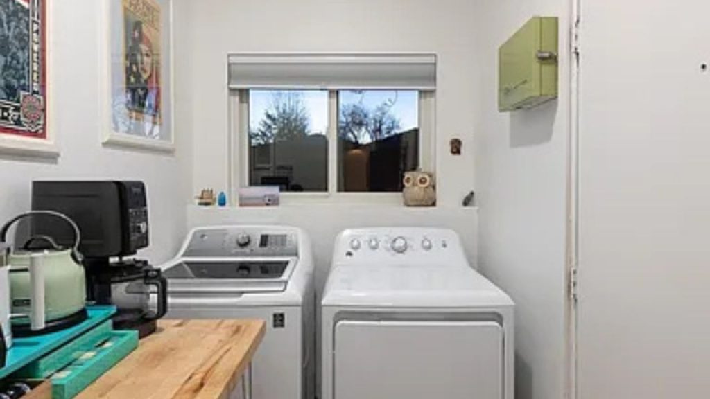 Bright laundry room with a washer, dryer, wooden countertop, and framed artwork.