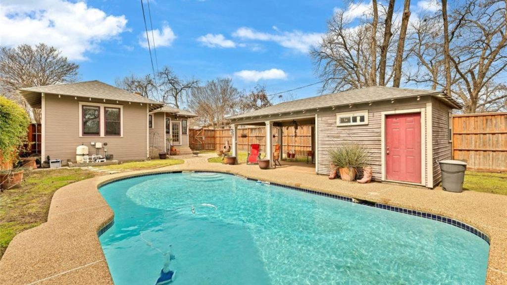 Backyard with a swimming pool, covered patio, and rustic outbuilding.