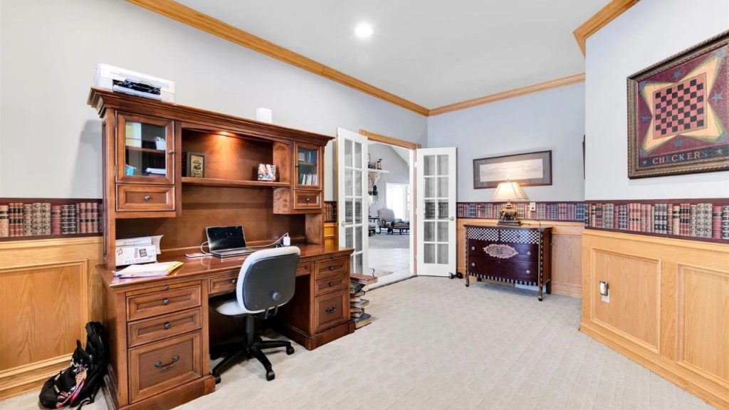 Elegant home office with wood paneling, built-in desk, and French doors.