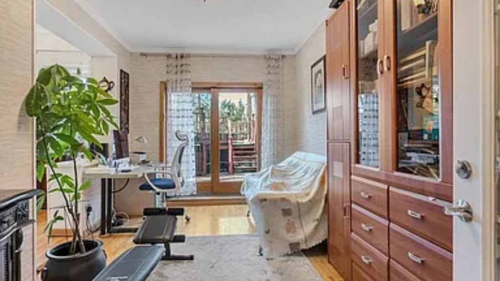 A fusion of work, leisure, and a dash of exercise, this warm room is a little bit of everything. A nicely lit home office space is located alongside the big glass doors, leading to an exterior deck, filling the room with lots of sunlight. A cozy couch is there for a lounge spot, while the wooden shelving unit contributes function and cohesiveness to the room. A soft area rug and potted plants introduce a cozy atmosphere, so the room does not feel unbalanced or unwelcoming. With an exercise bench hidden away, this room really has it all.