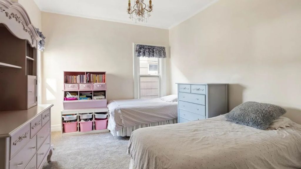 Soft-toned bedroom with two beds, vintage-style dressers, and a bookshelf.