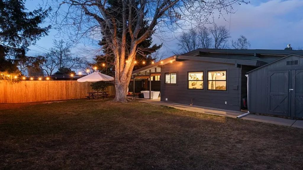 Cozy backyard at dusk with string lights, a picnic table, and a dark modern house.
