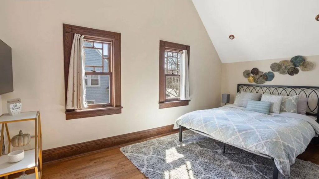 Bright bedroom with wood trim windows, a metal bed frame, and soft blue bedding.