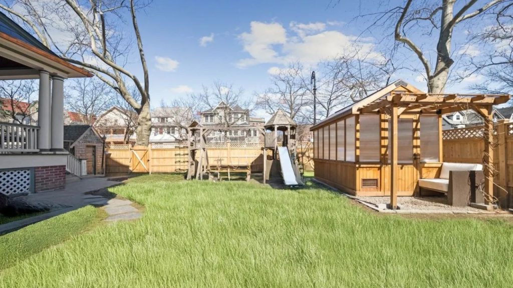 Spacious backyard with a wooden playset, greenhouse, and pergola-covered bench.