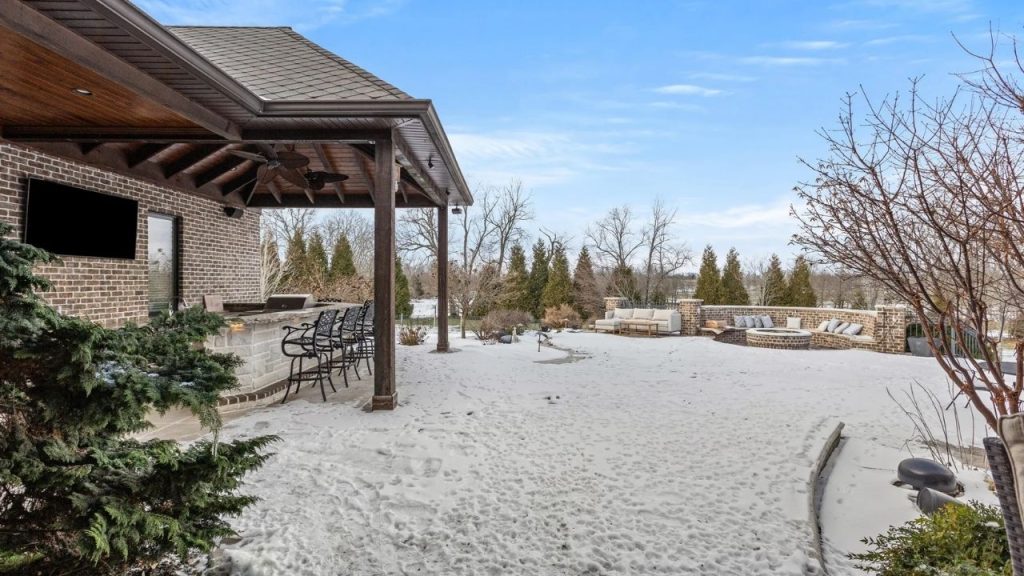 Backyard patio with bar, TV, and fire pit seating area in a snow-covered setting.