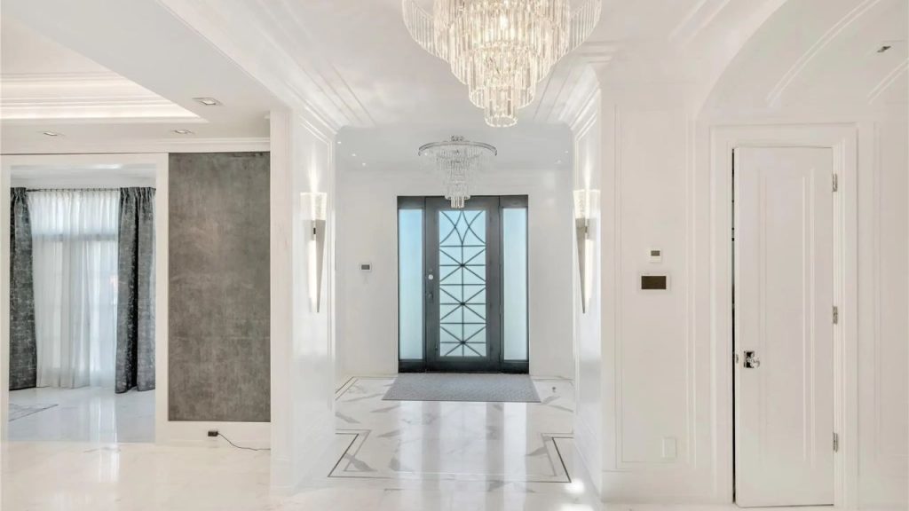 A grand foyer with marble floors, crystal chandeliers, and modern black double doors.