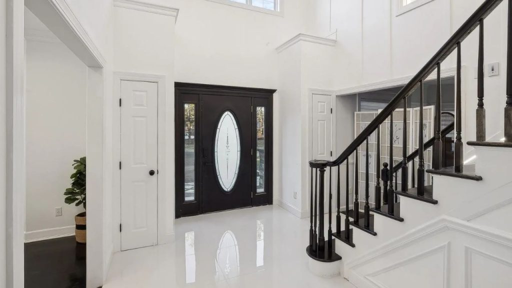 Bright foyer with a black front door, glossy white floors, and a dark wood staircase.