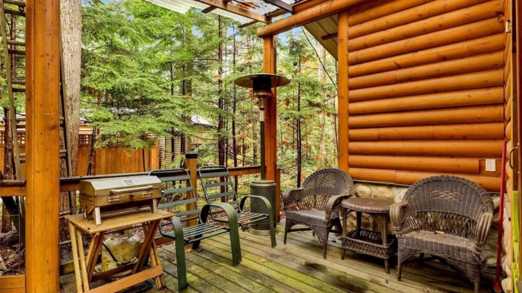 A rustic log cabin porch with wicker chairs, a grill, and forest views.