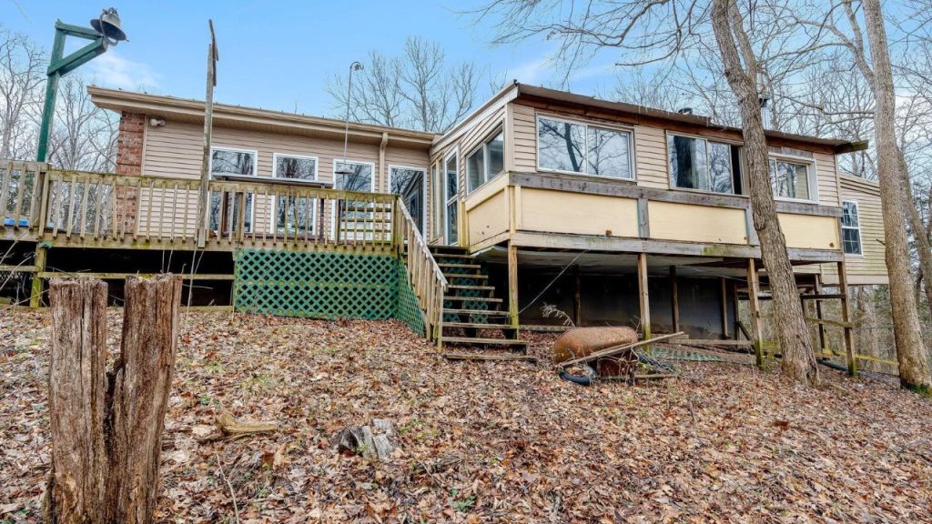 Elevated rustic home with a wooden deck and sunroom, nestled on a wooded hillside.