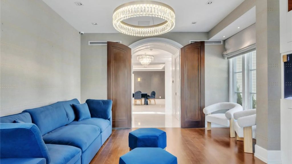 A stylish lounge with a blue sectional, crystal chandelier, and arched doorway leading to a dining area.