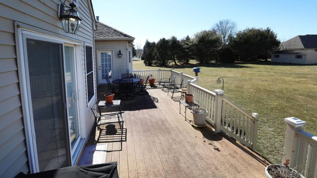 A wooden deck with outdoor furniture, planters, and a railing overlooking a large backyard.