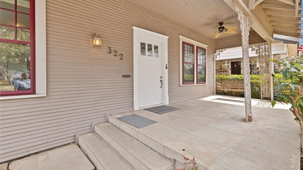 Covered front porch with a white door, red window frames, and decorative metal columns.