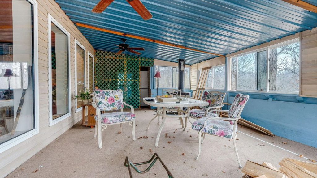Enclosed porch with floral patio furniture, a blue ceiling, and large windows overlooking the woods.