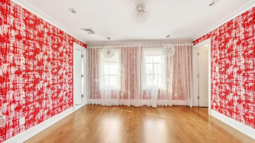 A bright room with red textured wallpaper, wood flooring, sheer white curtains, and modern pendant lights.
