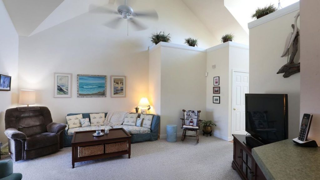 A bright living room with a coastal theme, featuring a sofa, recliner, TV, and vaulted ceilings.