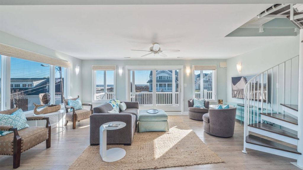A bright coastal living room with large windows, ocean views, and a spiral staircase.