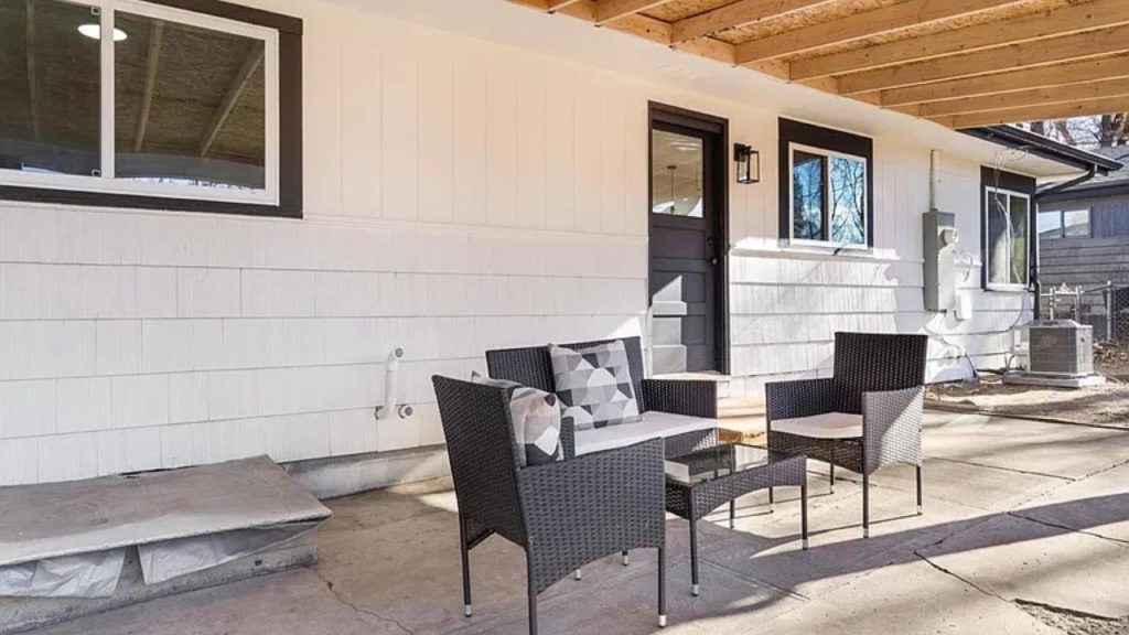 A covered patio with rattan seating, a wood ceiling, and a black-framed door leading inside.