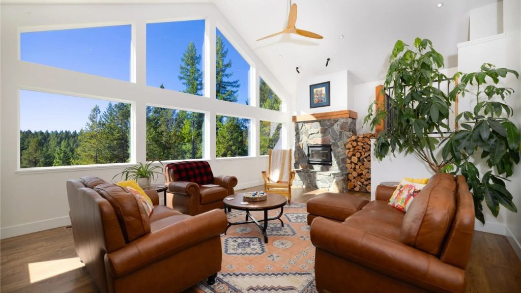A bright living room with large windows, a stone fireplace, and leather seating.