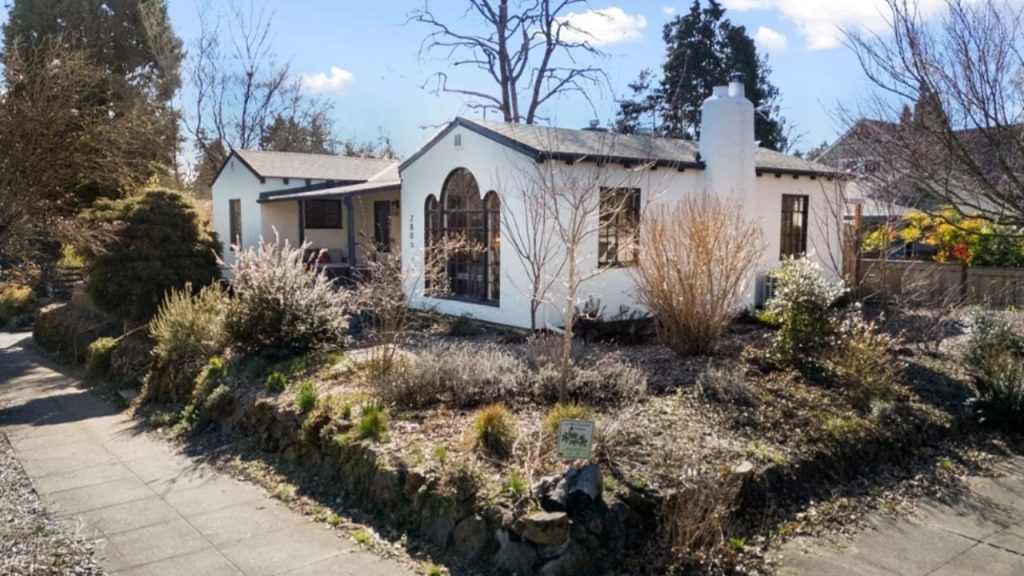 White Mediterranean-style house with arched windows, chimney, and landscaped front yard.