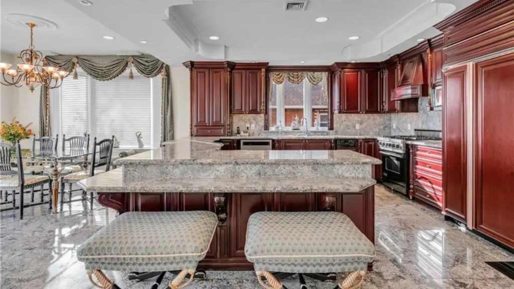 Classic kitchen with cherry wood cabinetry, granite countertops, ornate seating, and a red range, featuring a spacious dining area.