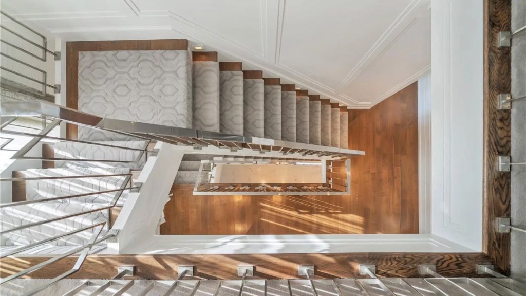 A modern staircase with a plush runner, wood steps, and sleek metal railings, viewed from above.