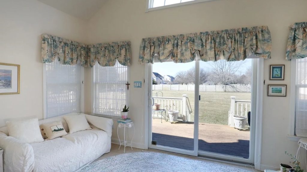 A bright sunroom with a cozy white sofa, large windows, and a view of the backyard.