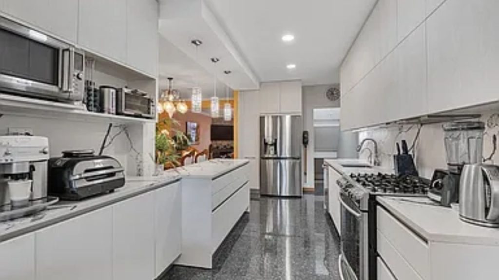 Modern white kitchen with stainless steel appliances and pendant lighting.