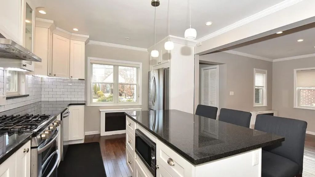 Modern kitchen with a black granite island, white cabinets, and stainless-steel appliances.