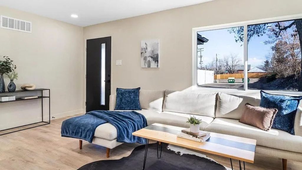 A modern living room with a neutral sectional, blue accents, and a large window letting in natural light.