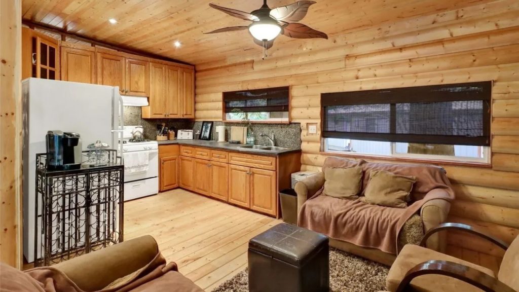Cozy log cabin kitchen with wood cabinets, plush seating, and warm lighting.