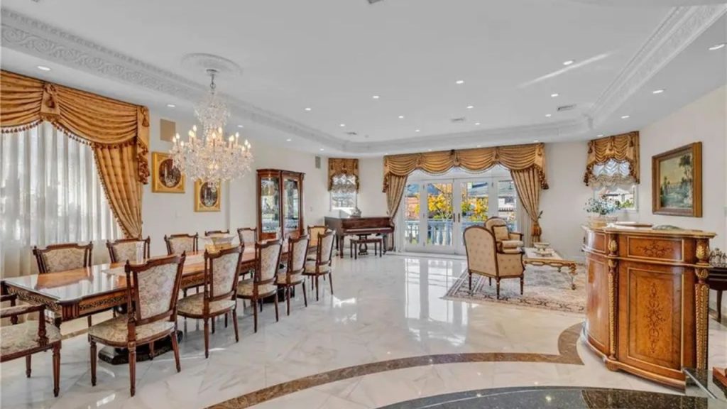 Elegant dining and lounge area with a grand chandelier, marble flooring, European-style furniture, and a grand piano near large French doors.