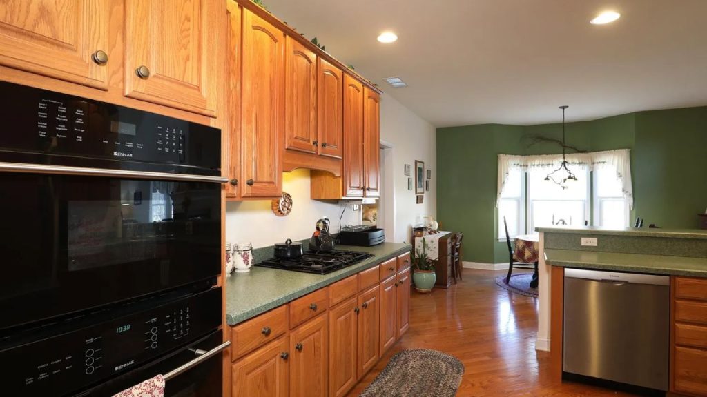 A warm kitchen with oak cabinets, green countertops, and a cozy dining nook with a bay window.