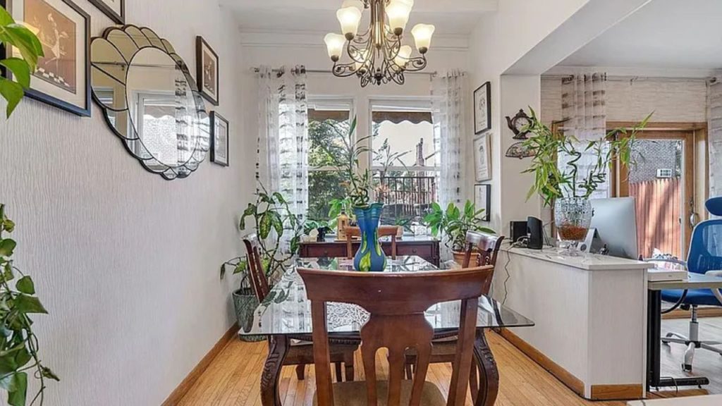 Well-lit dining area with glass table, wooden chairs, green plants, and a stylish chandelier.