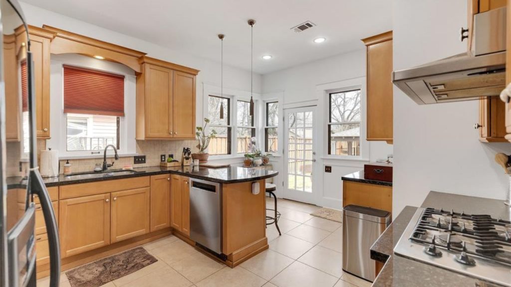 Bright kitchen with wood cabinets, black countertops, and a backyard view.