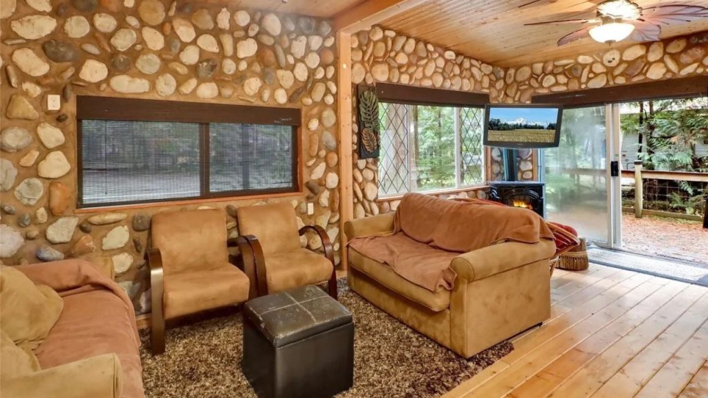 Rustic cabin living room with stone walls, cozy seating, and a wood stove.