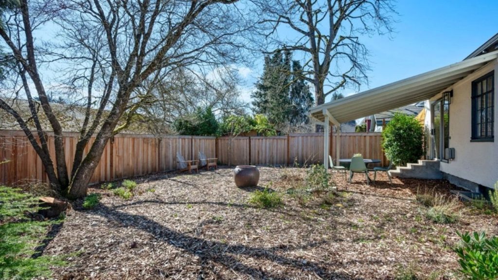 Backyard with a large tree, wooden fence, covered patio, and outdoor seating.