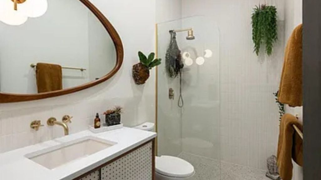 Warm and modern bathroom with wood accents, brass fixtures, and greenery.