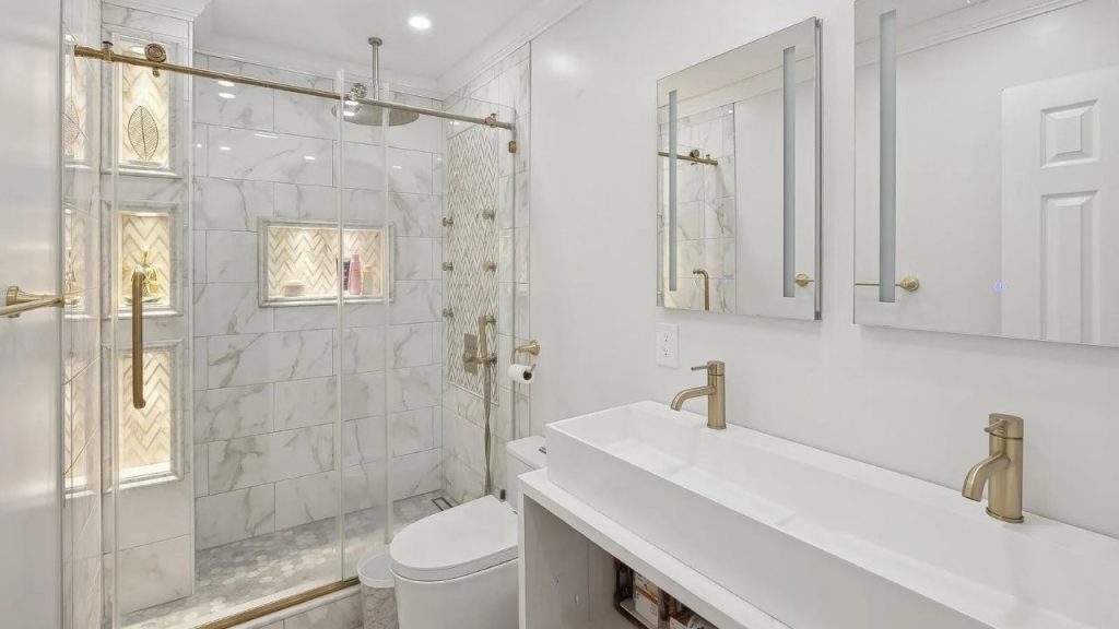 Elegant bathroom with marble walls, gold fixtures, and a glass-enclosed shower.