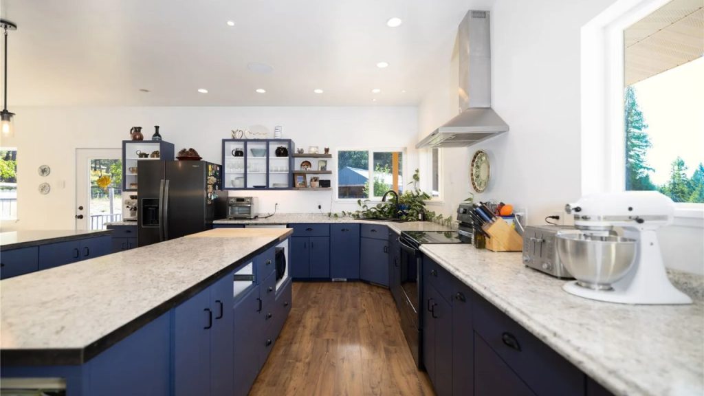 Bright kitchen with deep blue cabinets, marble countertops, and open shelving.