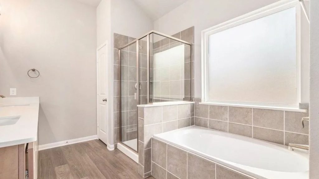 Modern bathroom with a glass shower, soaking tub, gray tiles, and wood-look flooring.