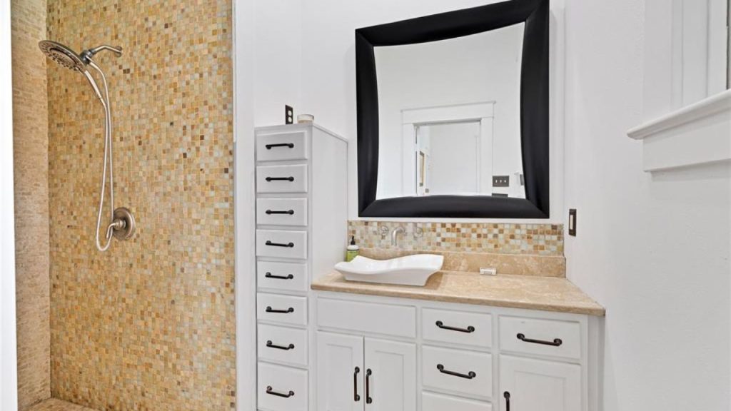 Modern bathroom with a mosaic-tiled shower, vessel sink, and stylish mirror.