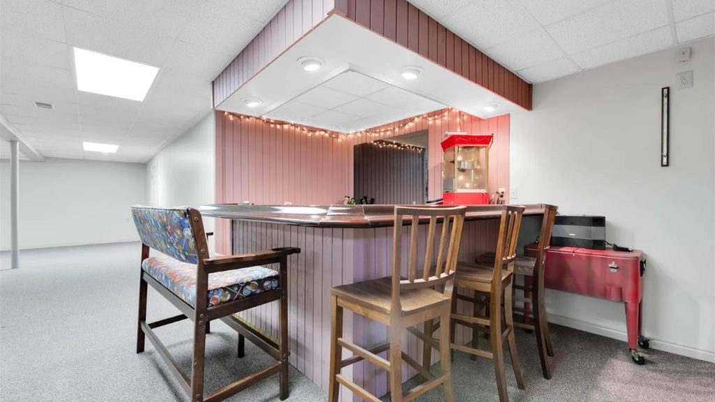 Basement bar with wood paneling, string lights, and seating.