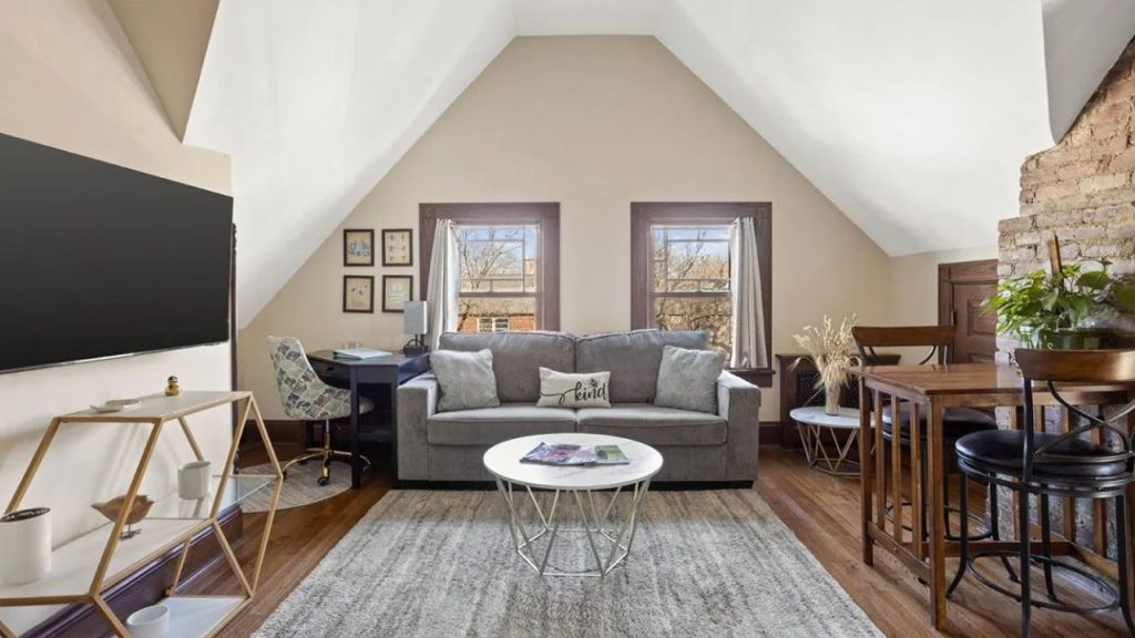 Loft-style living space with a gray sofa, workspace, and exposed brick wall.