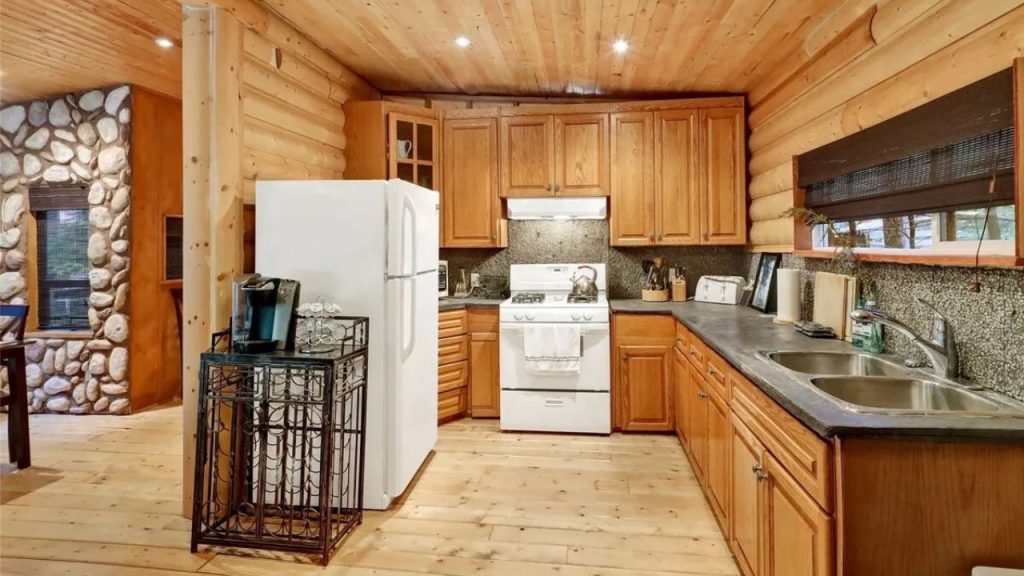 Rustic cabin kitchen with wood cabinets, white appliances, and warm lighting.
