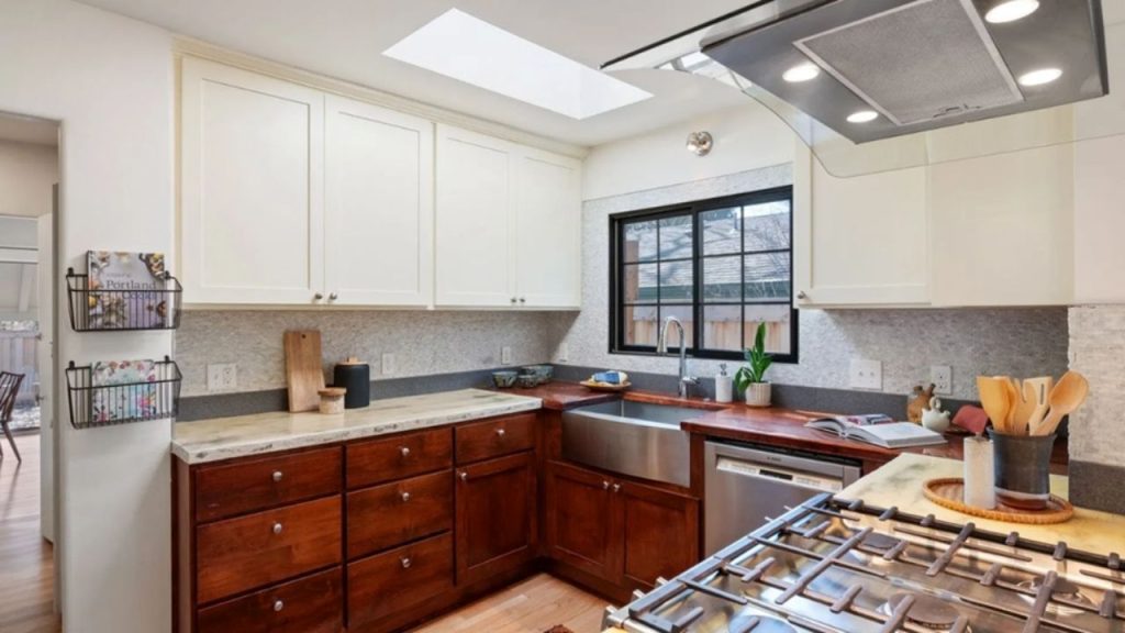 Kitchen with wooden lower cabinets, white upper cabinets, a skylight, and stainless steel appliances.
